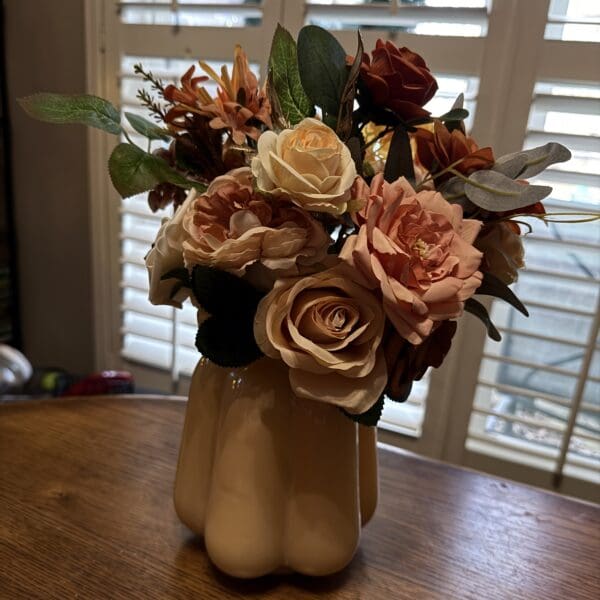 Elegant bouquet of blush and burgundy flowers in a white vase on a wooden table.