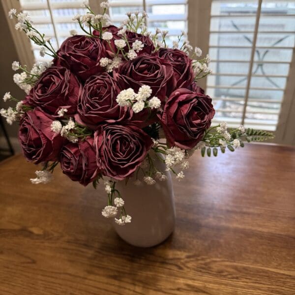 A bouquet of deep burgundy roses with white baby's breath in a vase.