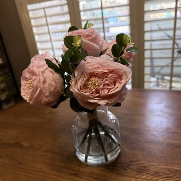 A small bouquet of pink roses in a glass vase on a wooden table.