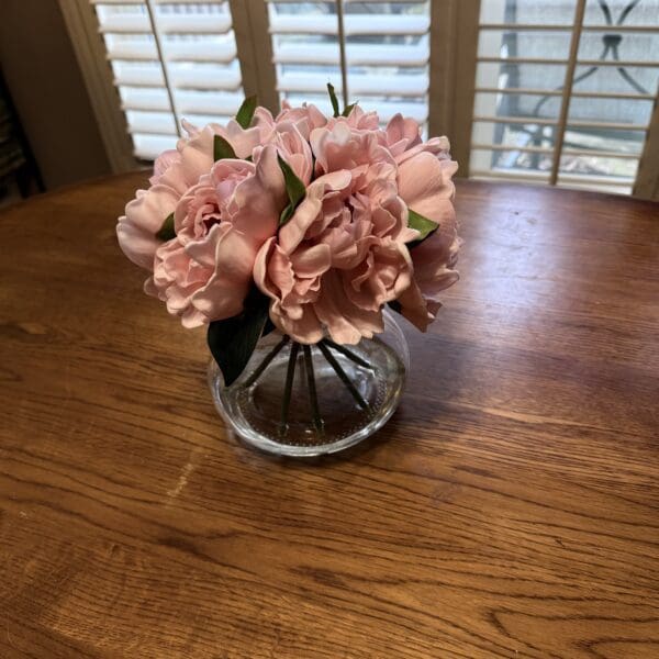 A small bouquet of pink flowers in a glass vase on a wooden table.