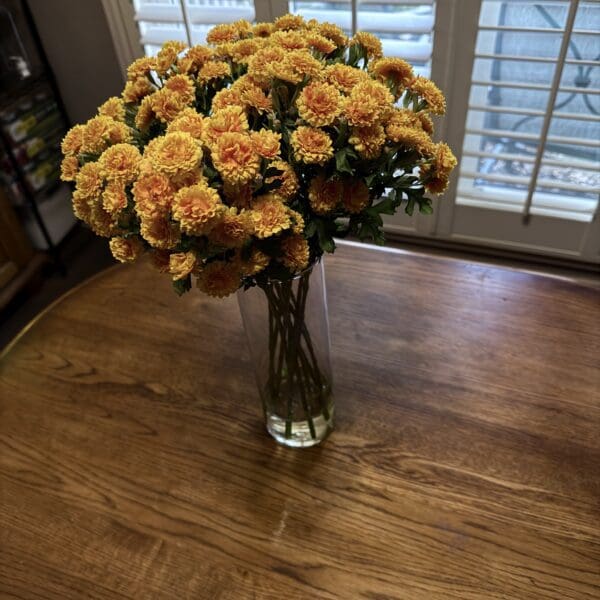 A bouquet of peach-colored carnations in a glass vase on a wooden table.