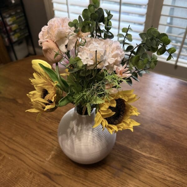 A bouquet of sunflowers and pink flowers in a white vase on a wooden table.