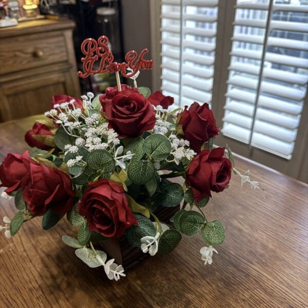A bouquet of red roses with greenery and white flowers on a wooden table.