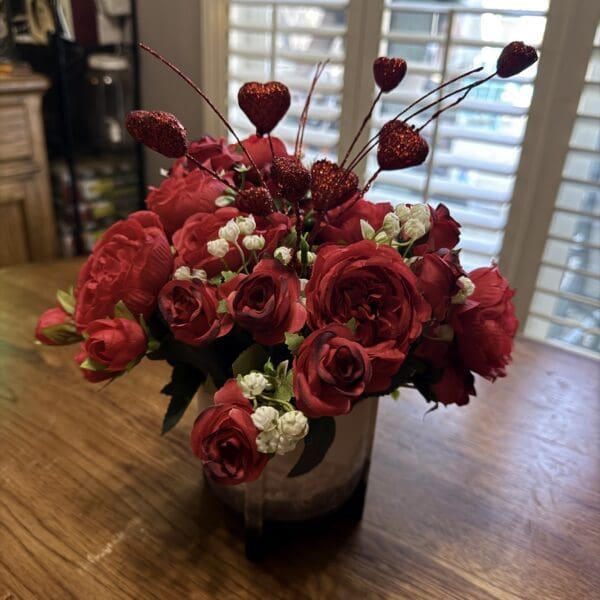 A vibrant bouquet of red roses in a white vase on a wooden table.