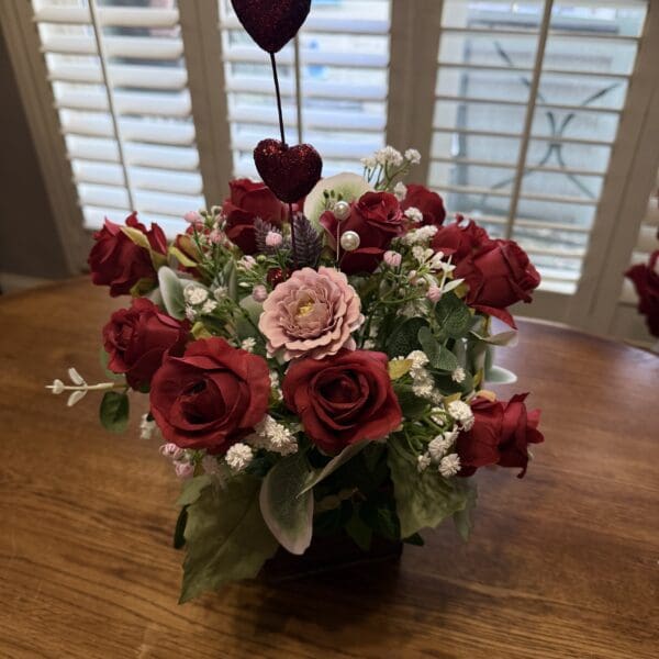 A bouquet of red and pink roses with baby's breath on a wooden table.