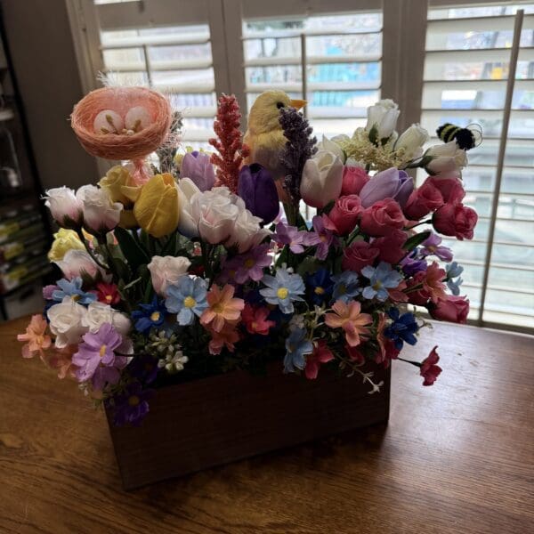 Colorful artificial flowers in a wooden box on a table by the window.