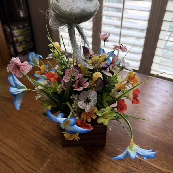 Colorful artificial flower arrangement in a blue basket on wooden table.