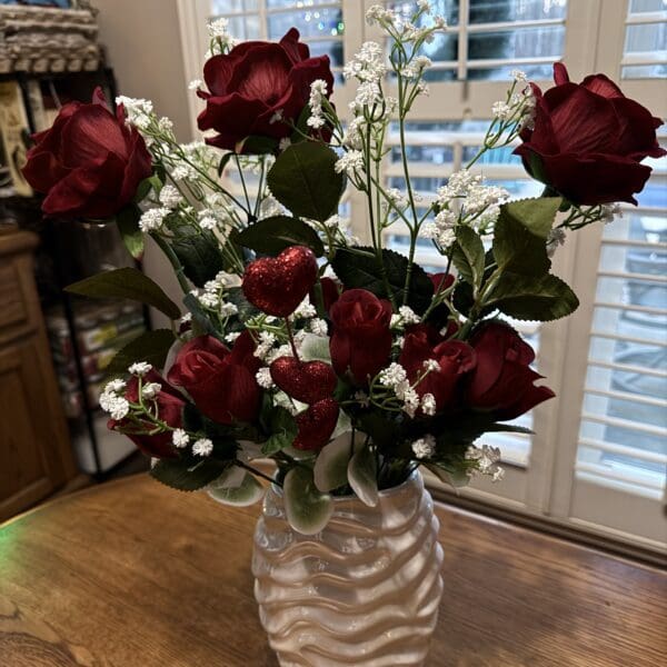 A bouquet of red roses in a white vase on a wooden table.