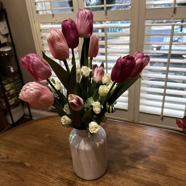 A vase with pink tulips and white flowers on a wooden table.