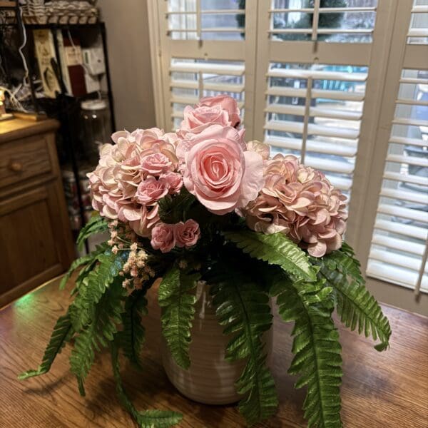 Elegant floral arrangement with pink roses, hydrangeas, and green ferns in a white vase.