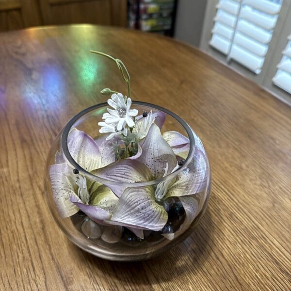 Glass bowl with white flowers on wooden table.