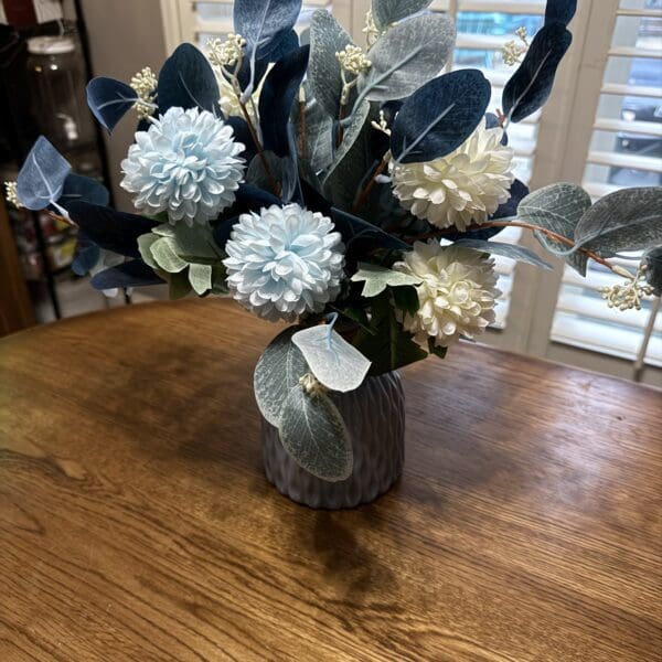 Elegant floral arrangement with white flowers and dark leaves in a rustic vase.
