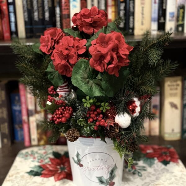 Red flowers in festive pot, bookshelf background.