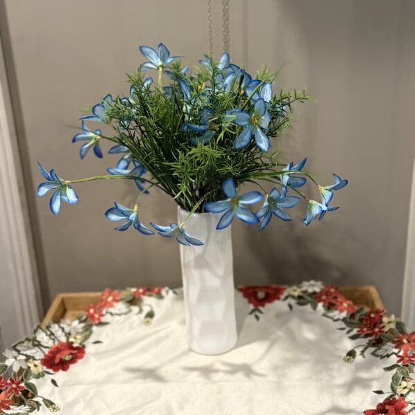 Blue flowers in white vase on table.